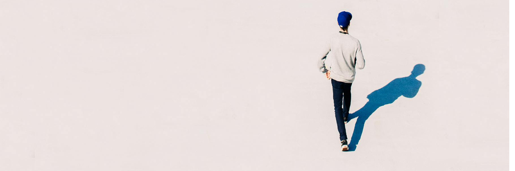 Person walking alone across a bright open space casting a long shadow — representing Brainchild’s journey of independent thought, clarity, and forward movement.