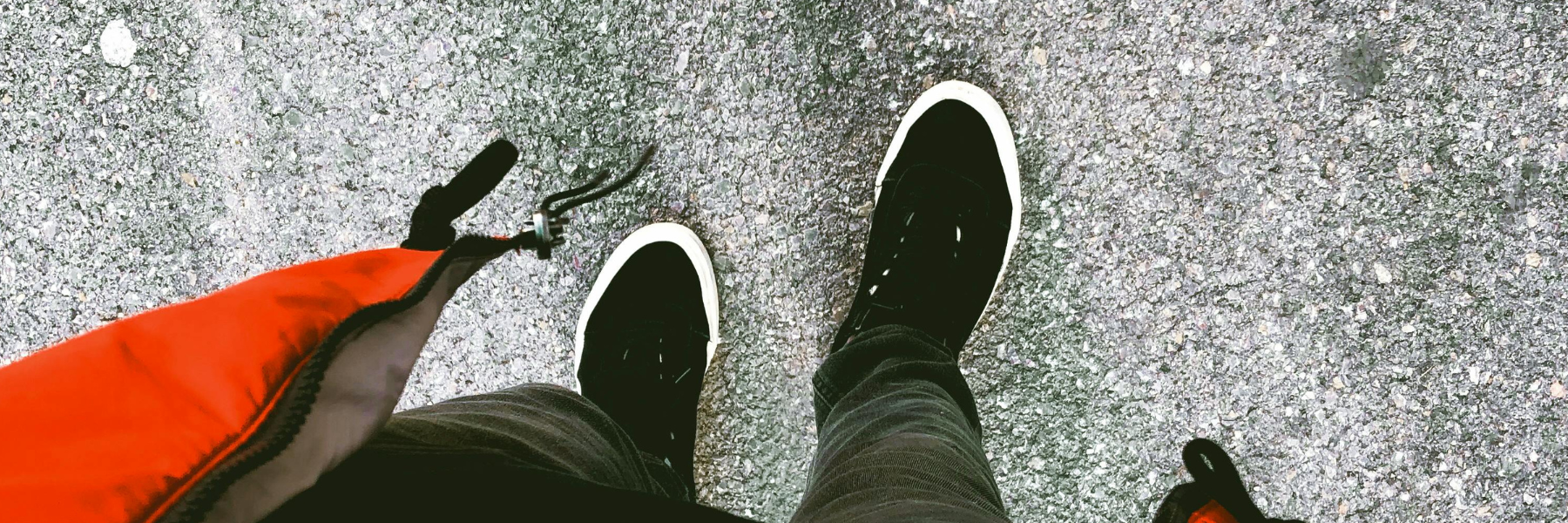 Top-down view of a person’s feet on pavement holding a red jacket — representing Brainchild’s grounded perspective, forward movement, and readiness for action.