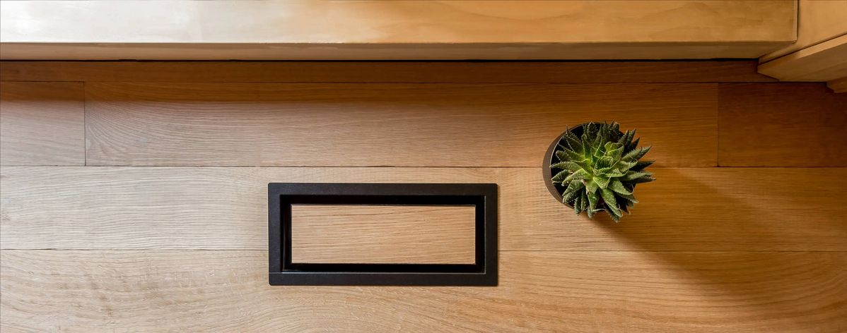 Minimalist wooden floor featuring a modern black rectangular Fittes floor vent beside a small potted succulent plant.
