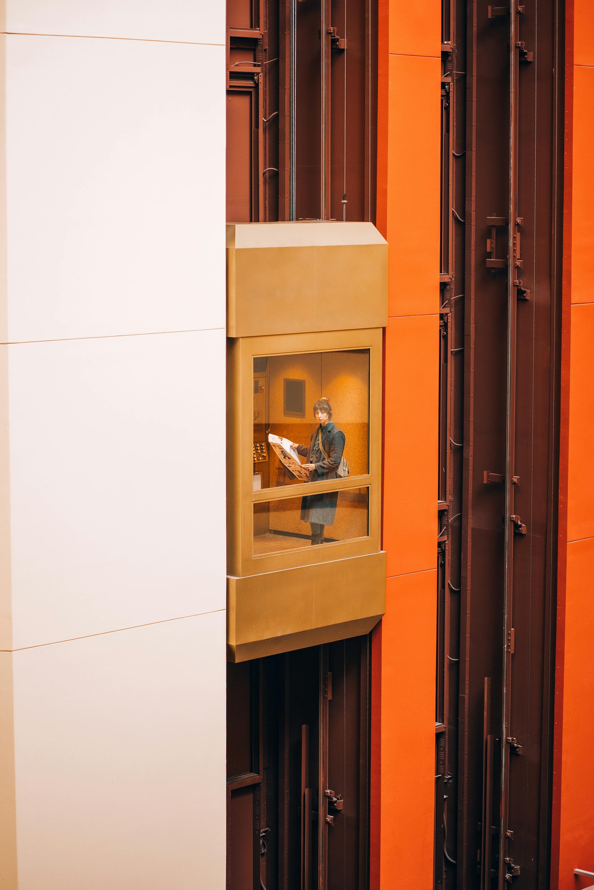 Person standing in a glass elevator reading a newspaper — symbolizing Brainchild’s upward movement, awareness, and thoughtful perspective in navigating modern systems.