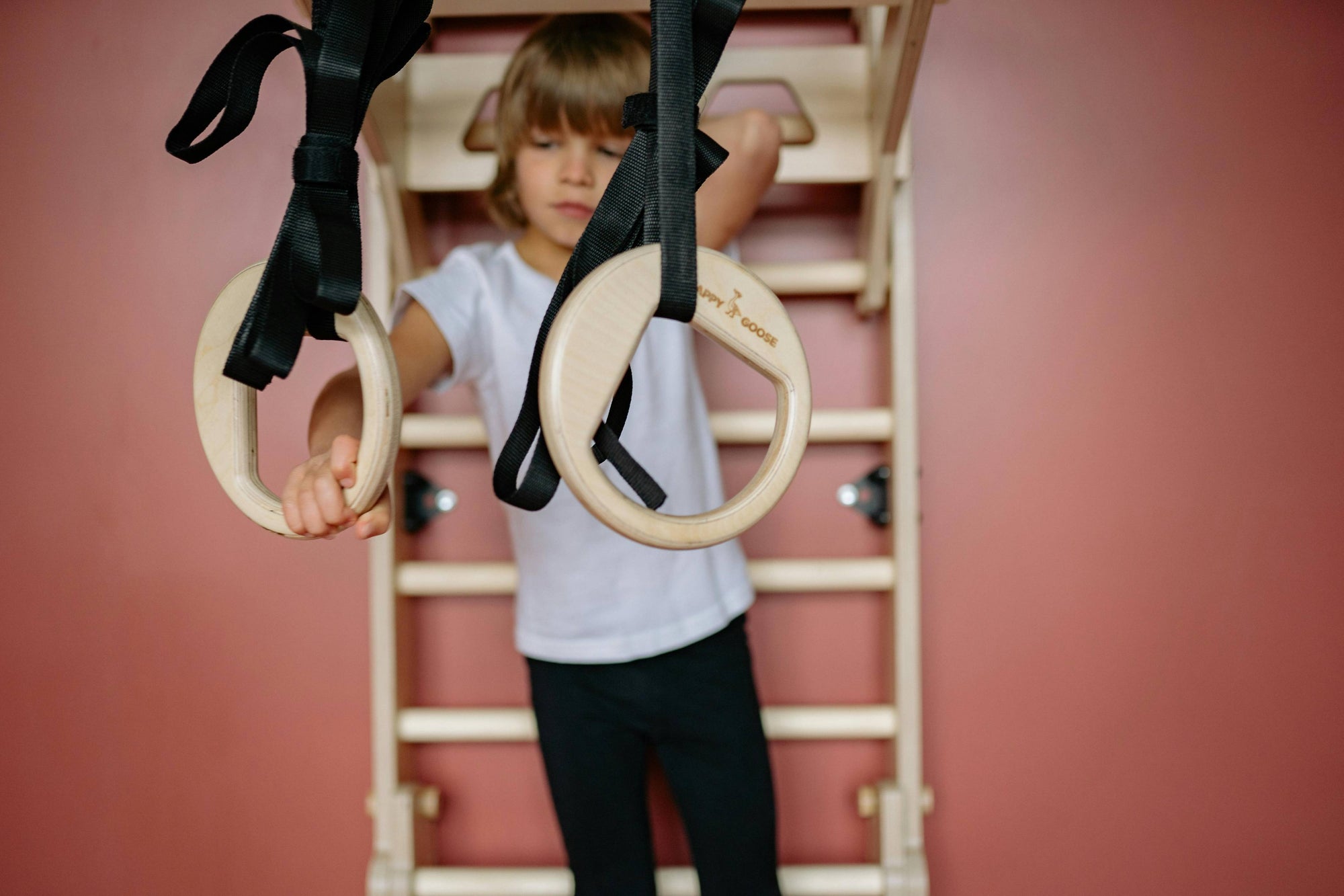 Child reaching for wooden gymnastic rings against a muted wall — representing Brainchild’s focus on growth, learning, and the discipline behind creative mastery.